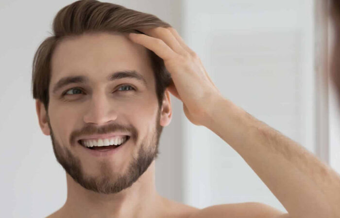 Young man with a beard smiles at his reflection while running his fingers through his hair in the mirror.
