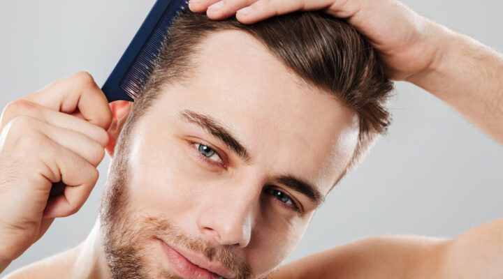 Man grooming his hair with a dark blue comb, tilting his head slightly as he styles.