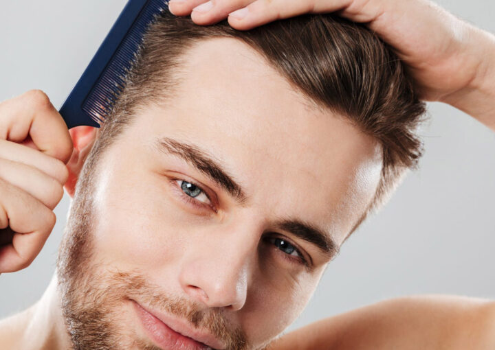 Man grooming his hair with a dark blue comb, tilting his head slightly as he styles.