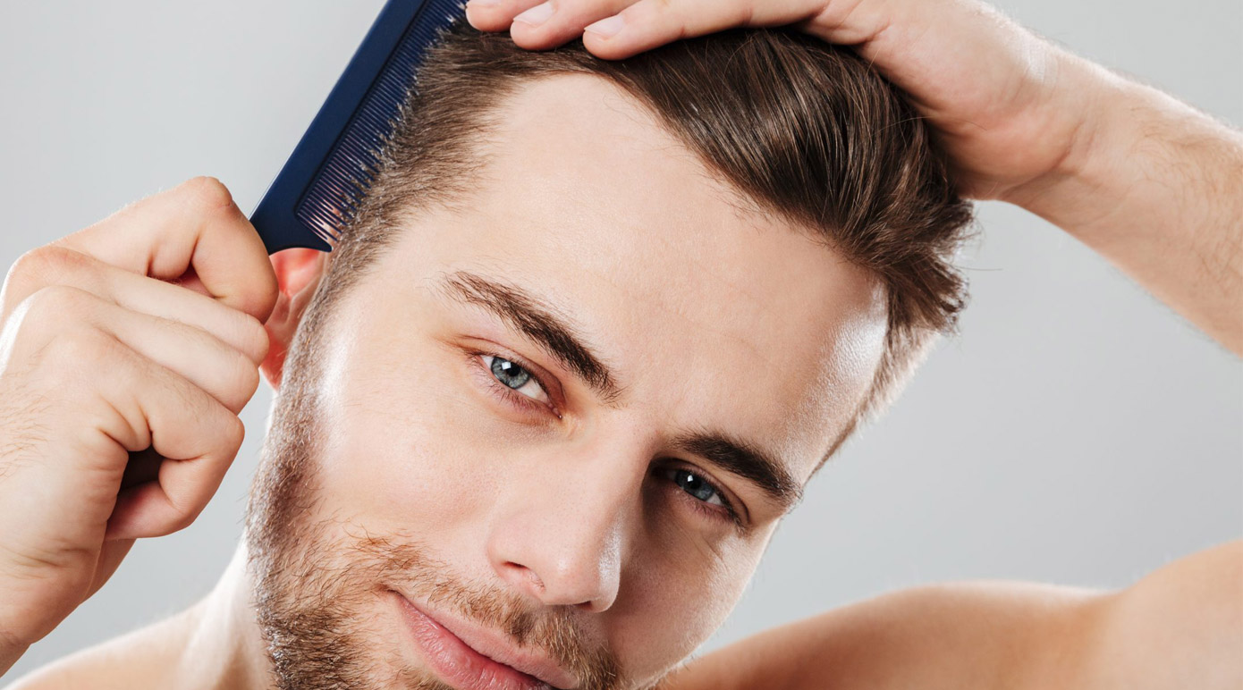 Man grooming his hair with a dark blue comb, tilting his head slightly as he styles.