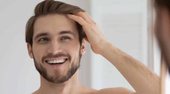 Smiling man with a beard touching his hair while looking at his reflection in a mirror.